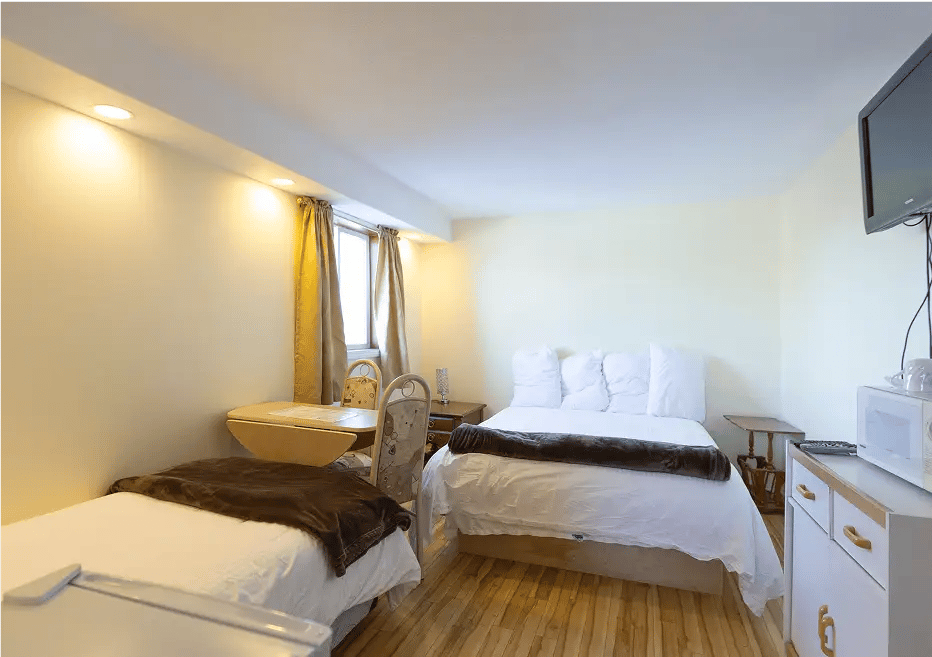 Queen and single beds with white covers, small table, TV.