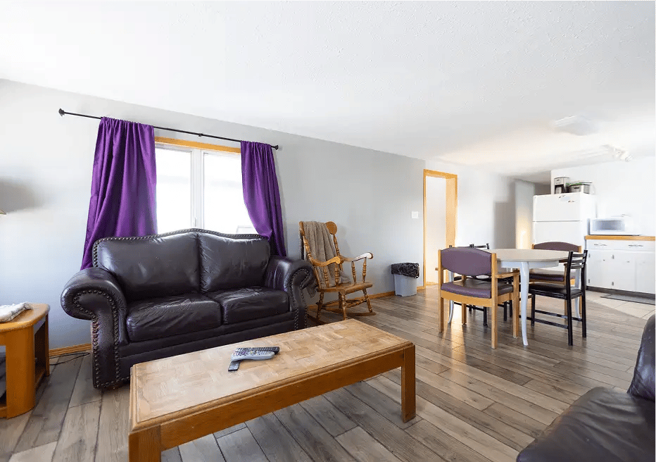 Main area, couch, purple curtains, table and kitchen in backgroud.